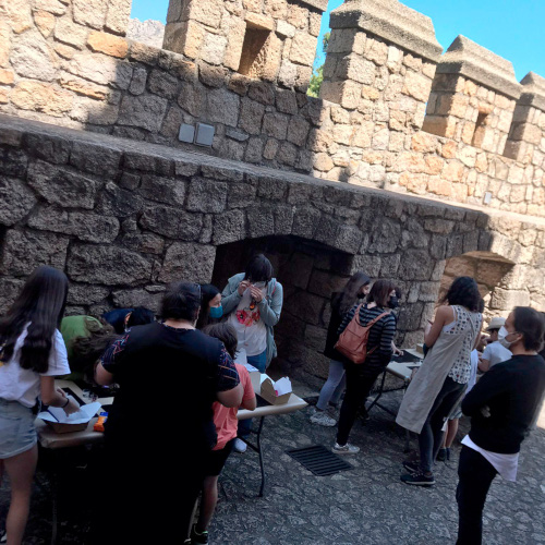 Bajo una muralla, un grupo de personas analiza en dos mesa soportes de piezas patrimoniales.